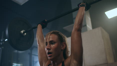 a-female-weightlifter-performs-a-barbell-lift-in-a-dark-gym.-a-woman-lifting-a-heavy-bar-over-her-head